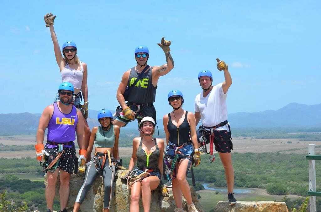 Group of people in helmets and harnesses posing on a hilltop before a zipline adventure.