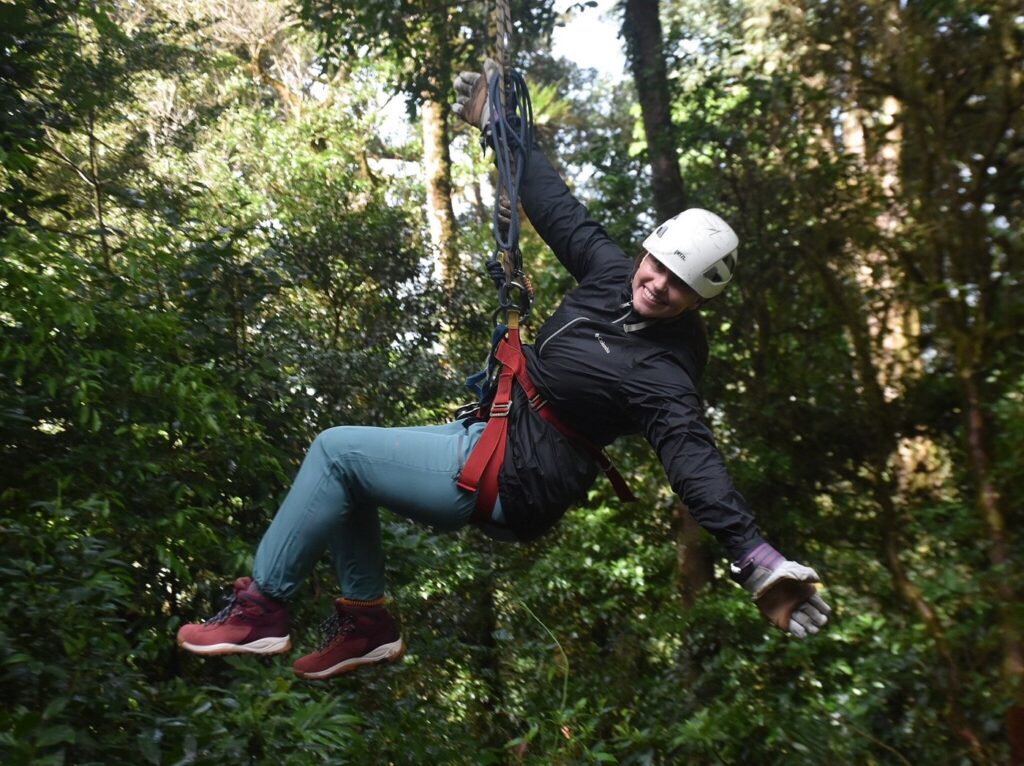 Person ziplining through a lush rainforest, wearing a helmet and safety harness.