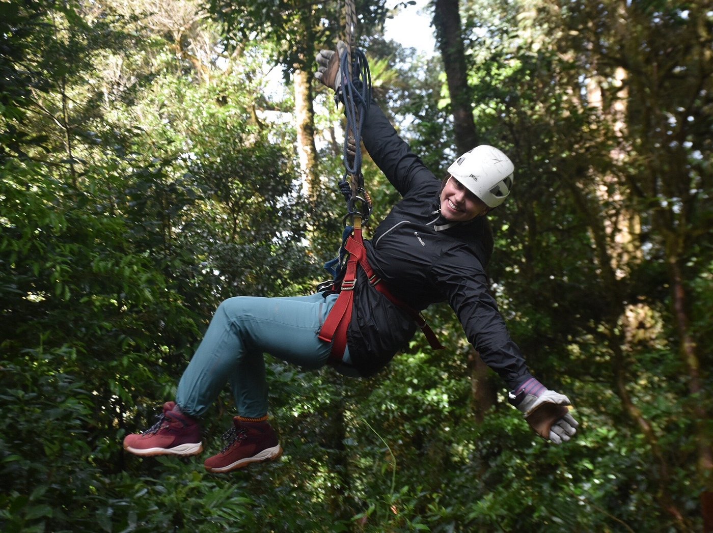 Person ziplining through a lush rainforest, wearing a helmet and safety harness.