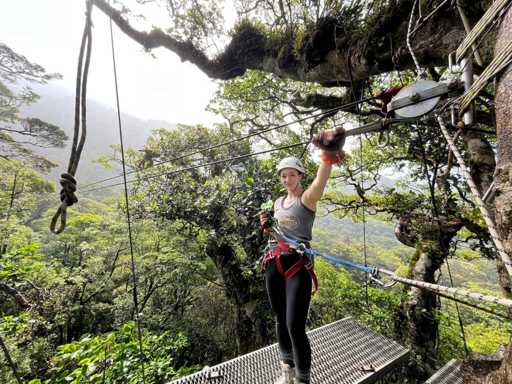 Girl standing on a rainforest canopy platform wearing zipline safety gear.