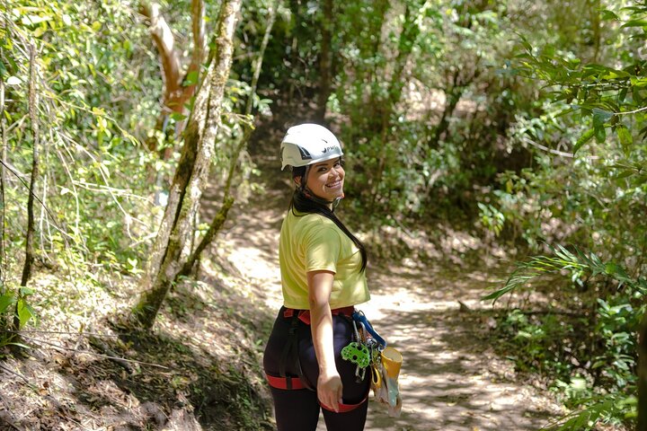 A ziplining participant wearing a helmet, fitted shirt, leggings, and safety harness.