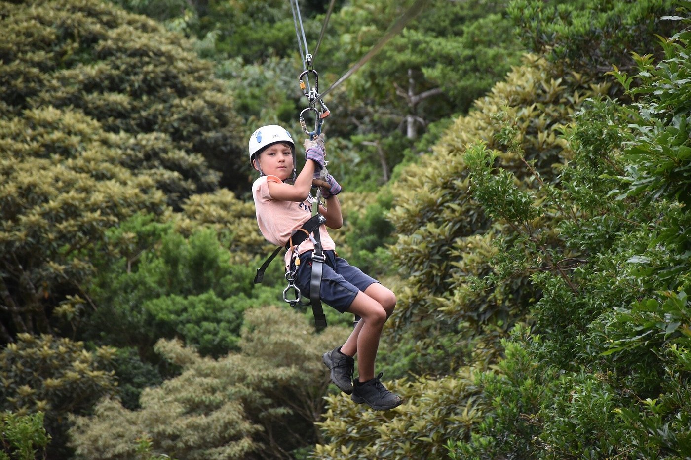 Child wearing a helmet and safety harness ziplining above dense green forest in Costa Rica.