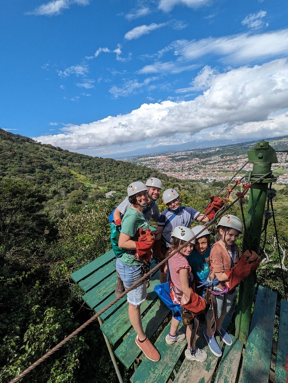 Family wearing helmets and safety harnesses gather on a treetop zipline platform in Costa Rican.