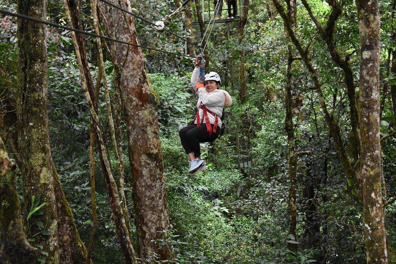 Person ziplining high above the Costa Rica rainforest canopy surrounded by lush tropical forest.