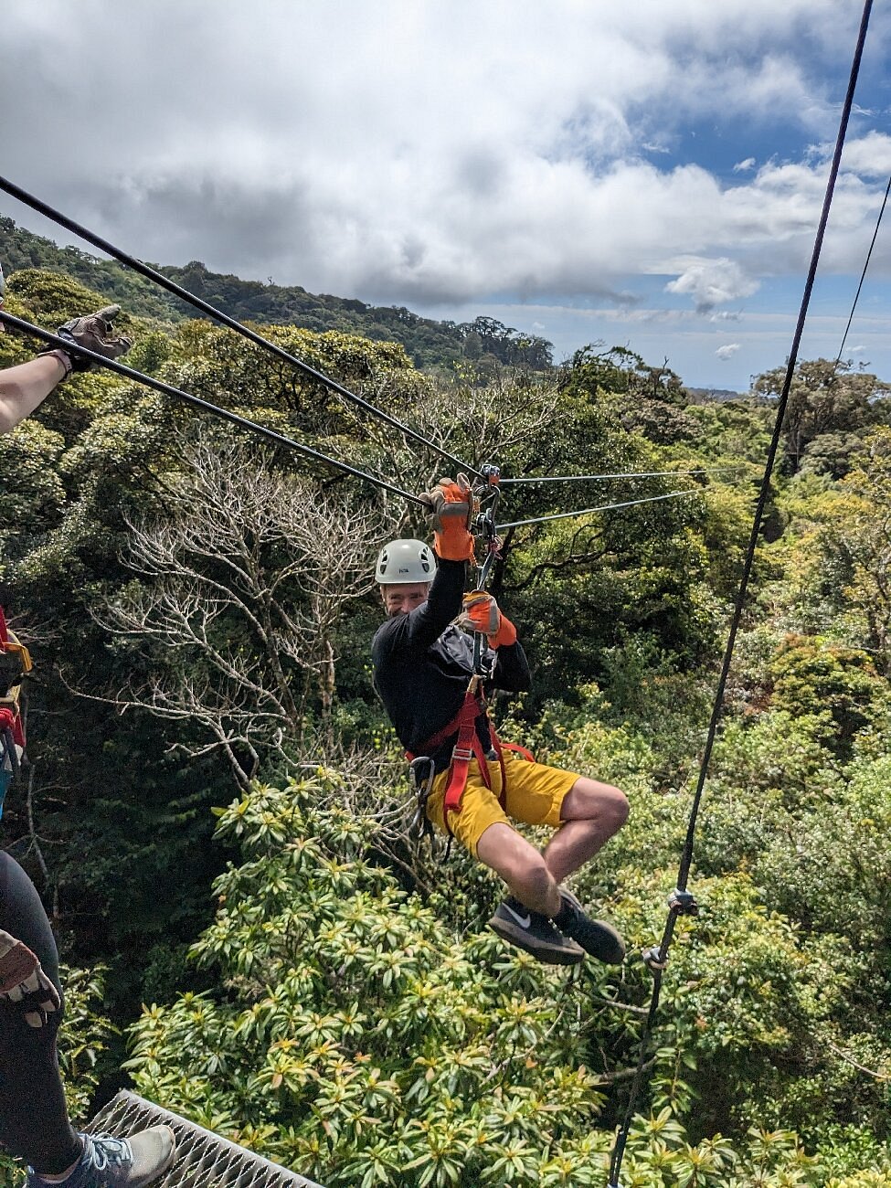 Zipliner wearing a helmet and harness glides above Costa Rica’s dense green forest canopy.