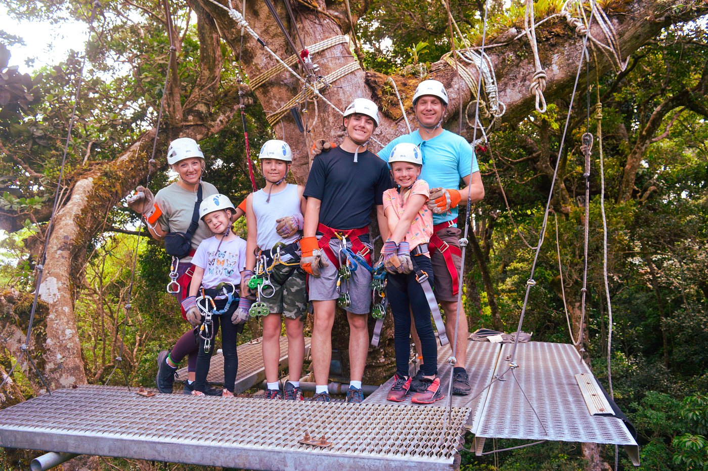 Family wearing zipline harnesses poses on a treetop platform in a Costa Rican forest.