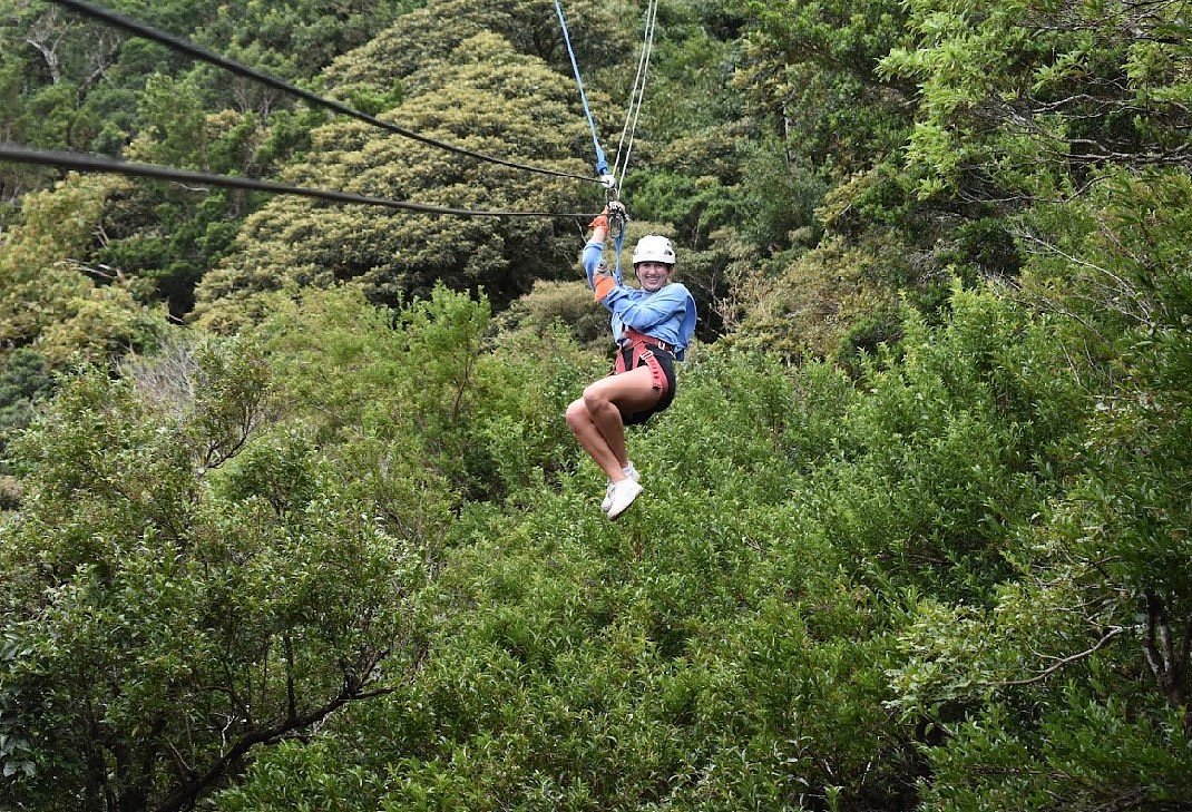 Person wearing a helmet and safety harness ziplining above dense green forest in Costa Rica.