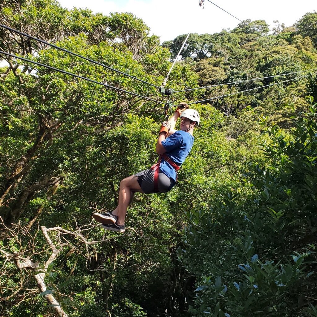 Woman ziplining through dense green forest wearing helmet and harness.