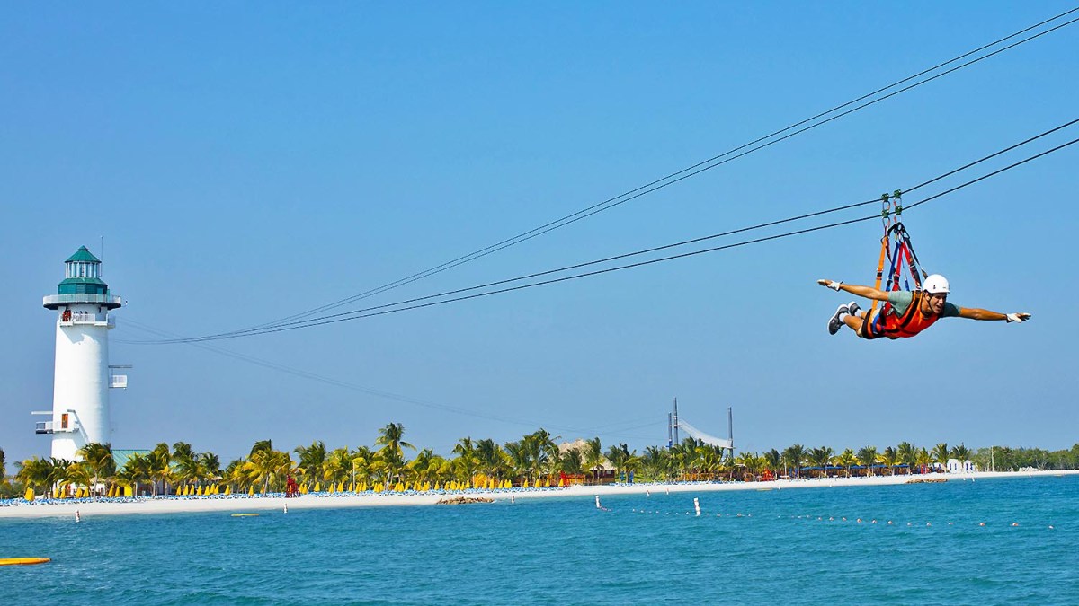 Zipliner soars over turquoise water beside a tropical island lighthouse