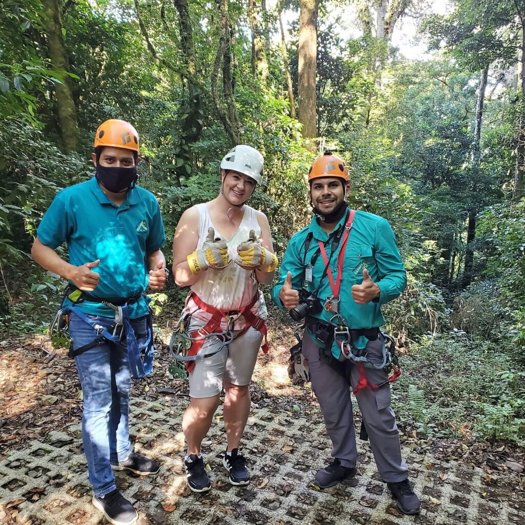 Traveler with two zipline guides wearing helmets and harnesses in a Costa Rica rainforest.